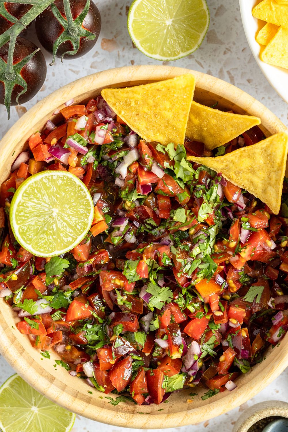 Fresh homemade pico de gallo salsa in a wooden bowl topped with lime and tortilla chips.