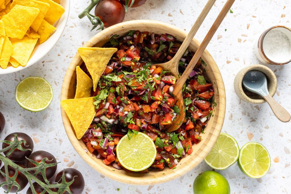 Fresh homemade pico de gallo salsa in a wooden bowl with tortilla chips and lime wedges on a white surface.