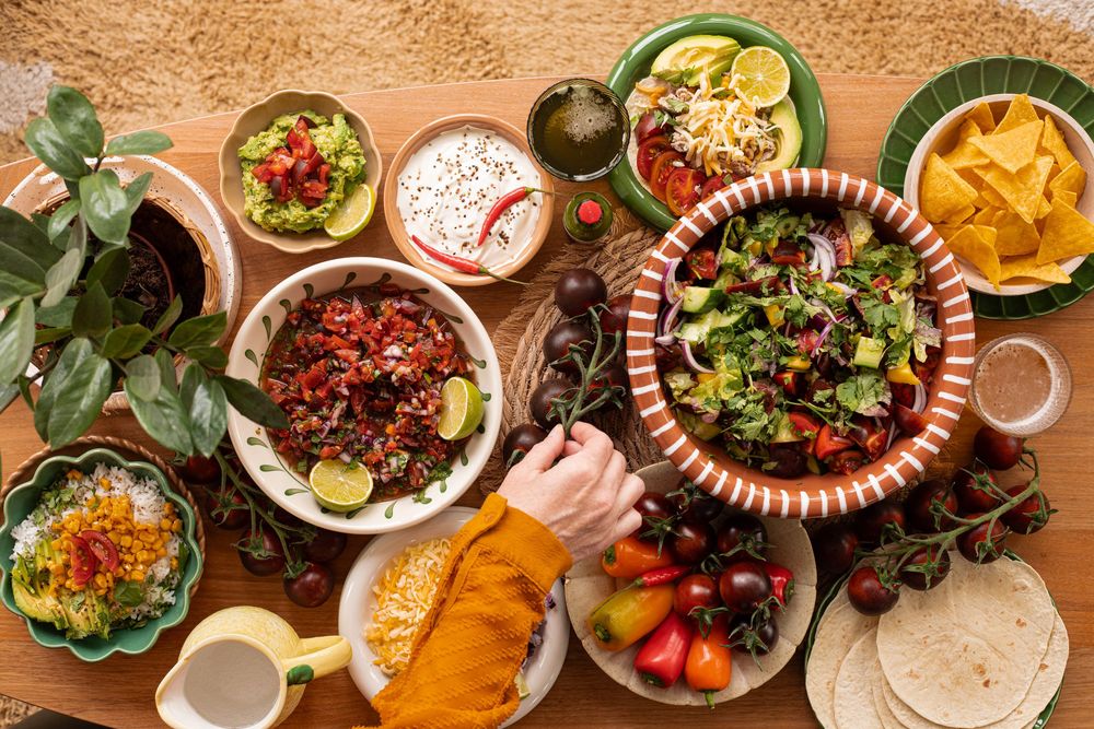 Colorful Mexican food spread with salads, salsas, tortillas, nachos, and fresh ingredients on a wooden table.