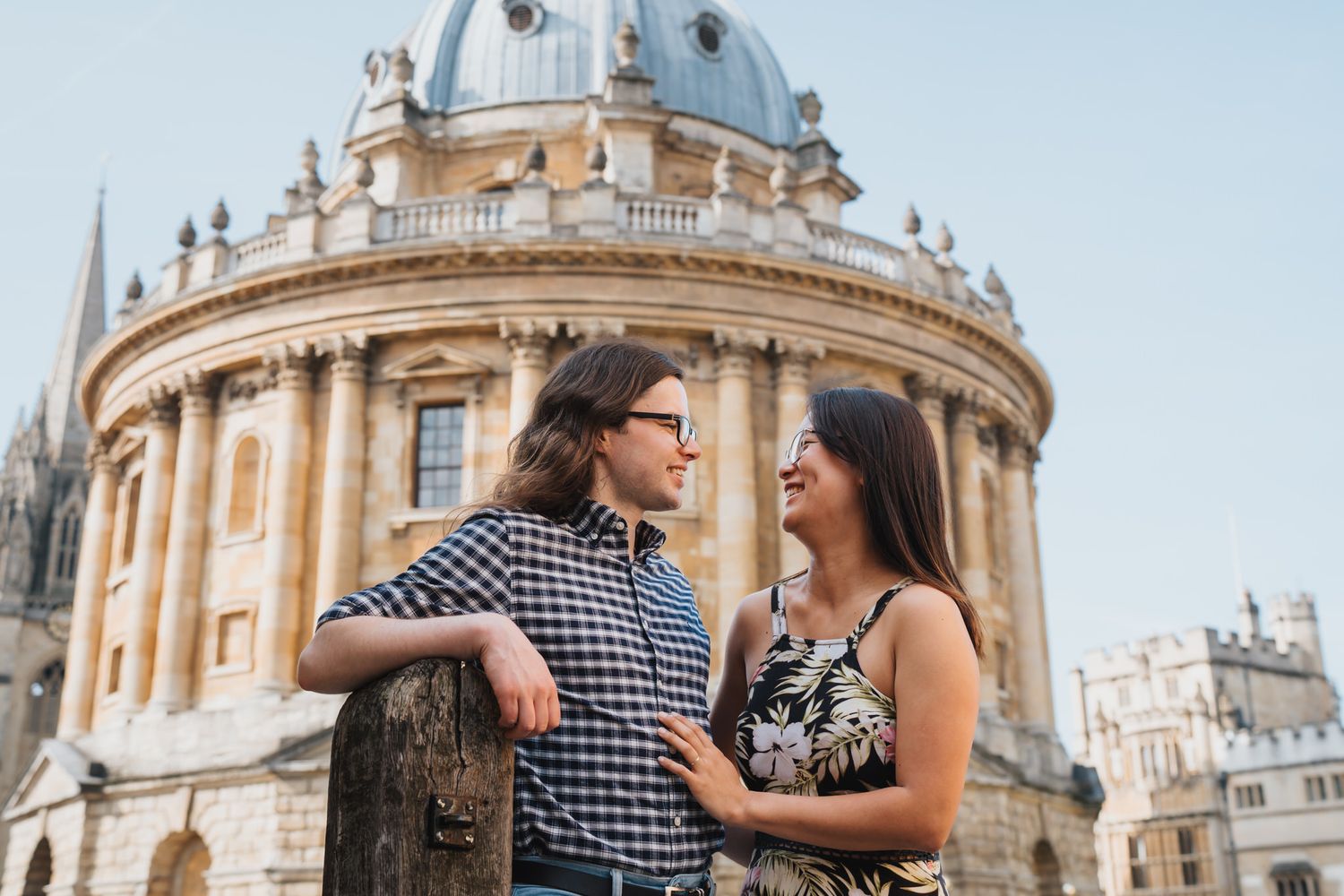 Couple smiling at each other in front of the Radcliffe Camera, Oxford, on a sunny day.