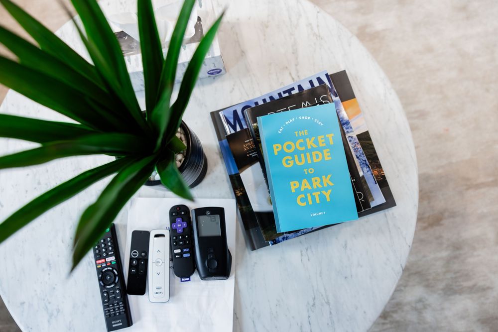 Pocket Guide to Park City book with remote controls and green plant on marble coffee table.