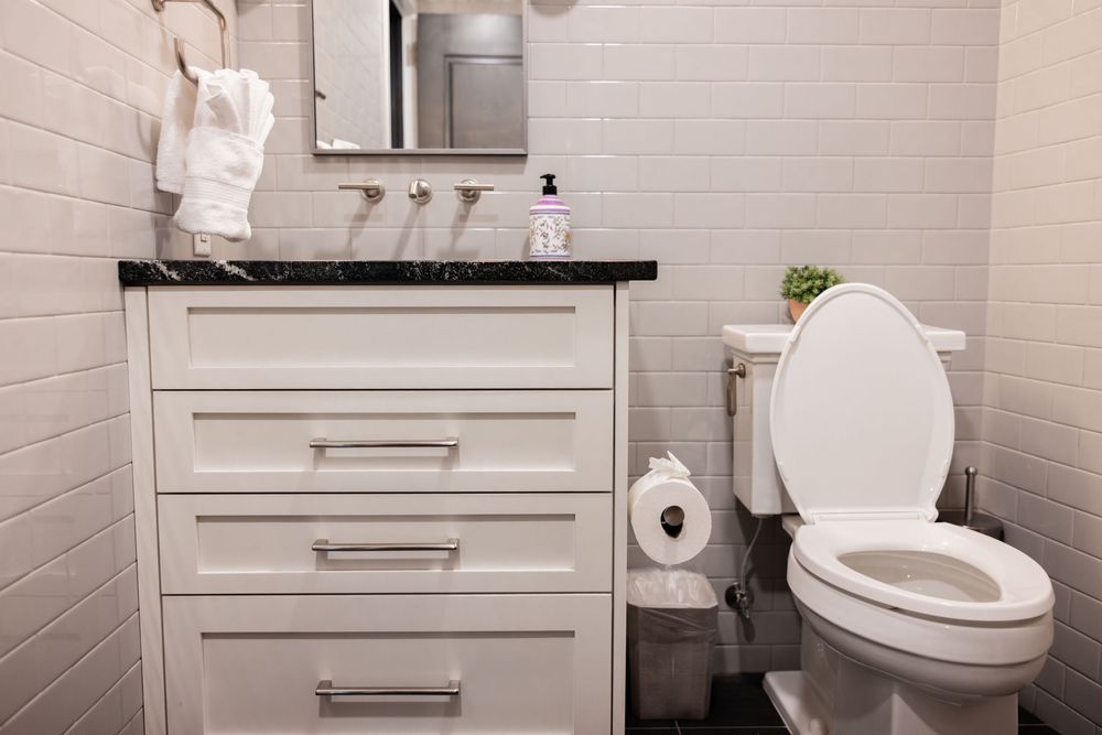 Modern white bathroom with marble-top vanity, subway tile walls, and clean toilet with spare roll holder.