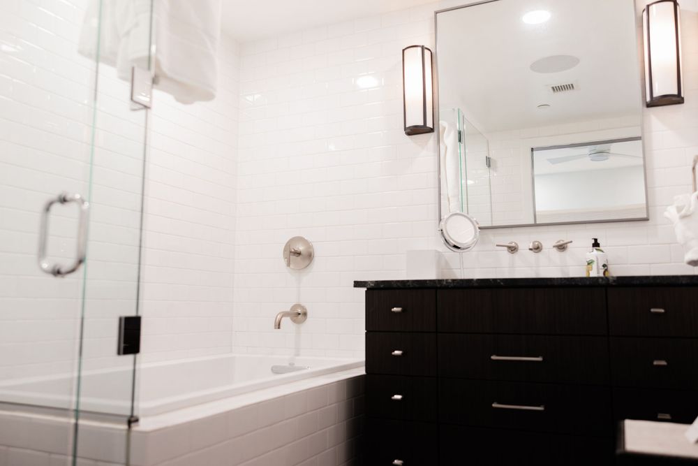 Modern bathroom with black vanity, white subway tile, soaking tub, glass shower, and wall sconces flanking a large mirror.