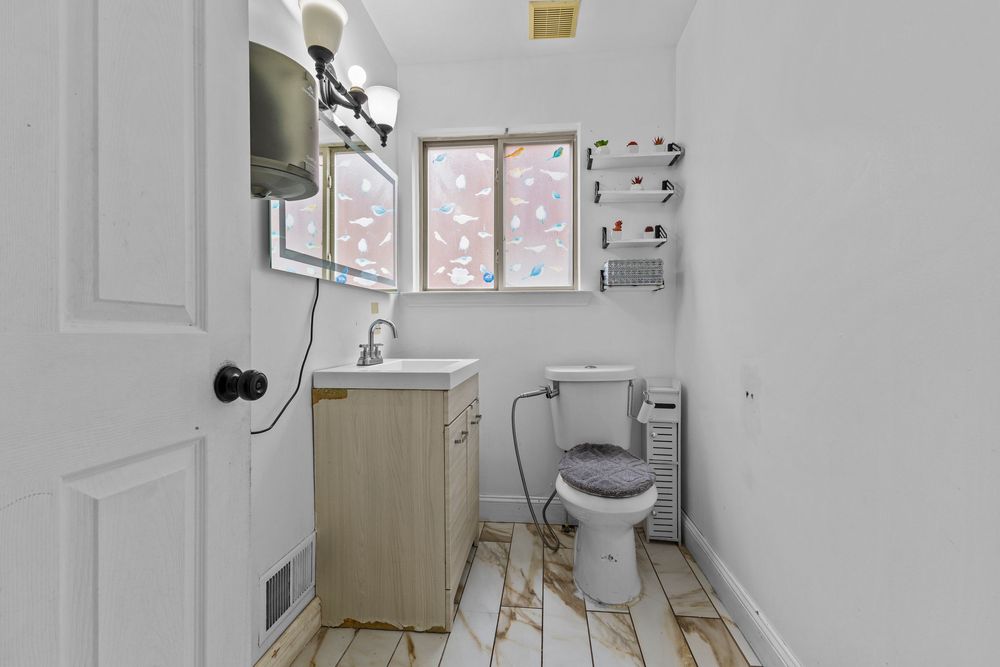 Small white bathroom with pedestal vanity, toilet, and frosted window providing natural light.