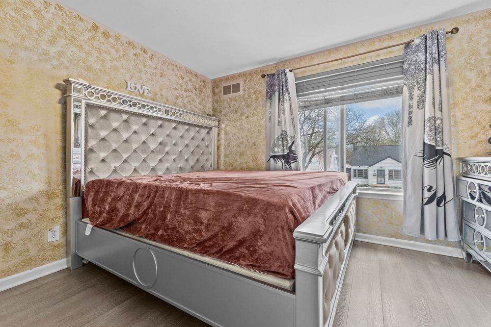 Bedroom with ornate upholstered headboard, pink bedding, wallpaper accent walls, and natural window light.