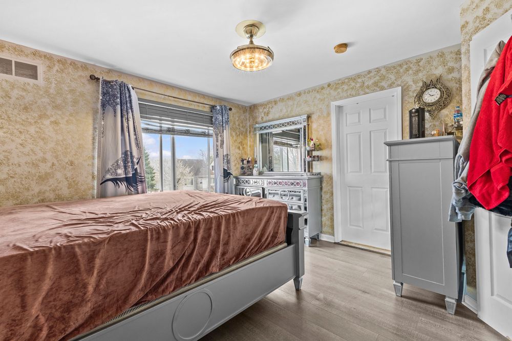 Bedroom with decorative wallpaper, gray bed frame, chandelier lighting, and bright natural window light.