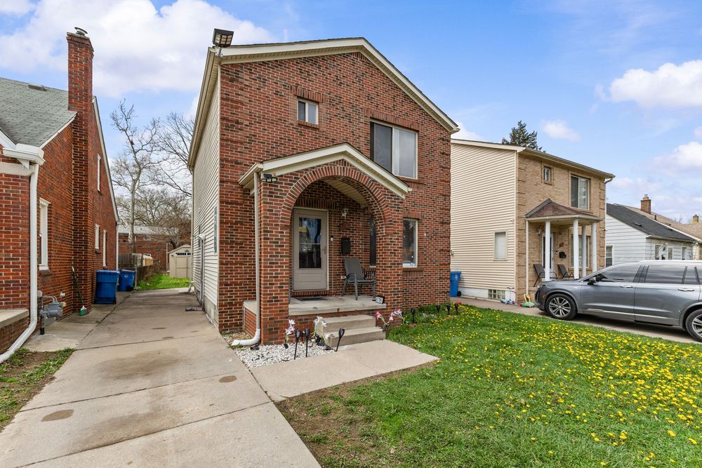 Brick two-story home with arched entryway, manicured lawn, and concrete driveway in a residential neighborhood.