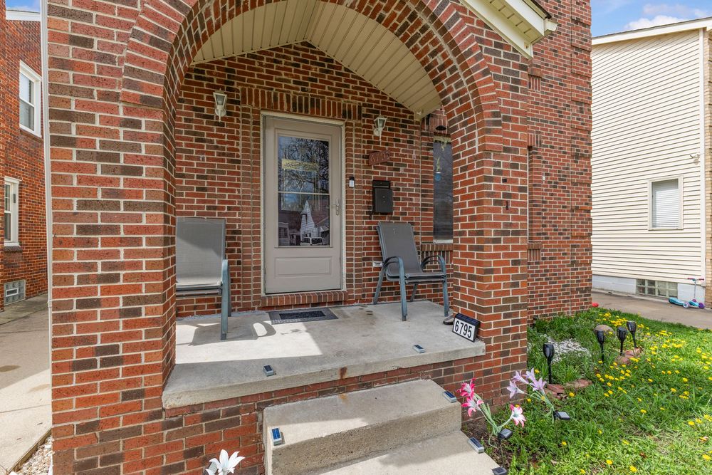 Charming brick arched front porch entrance with decorative columns, seating, and glass front door.