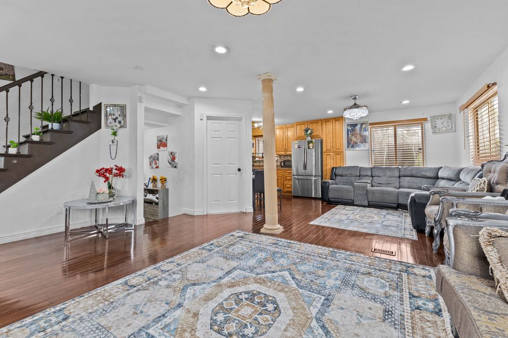 Open living room with hardwood floors, decorative column, staircase, recessed lighting, and view to kitchen.