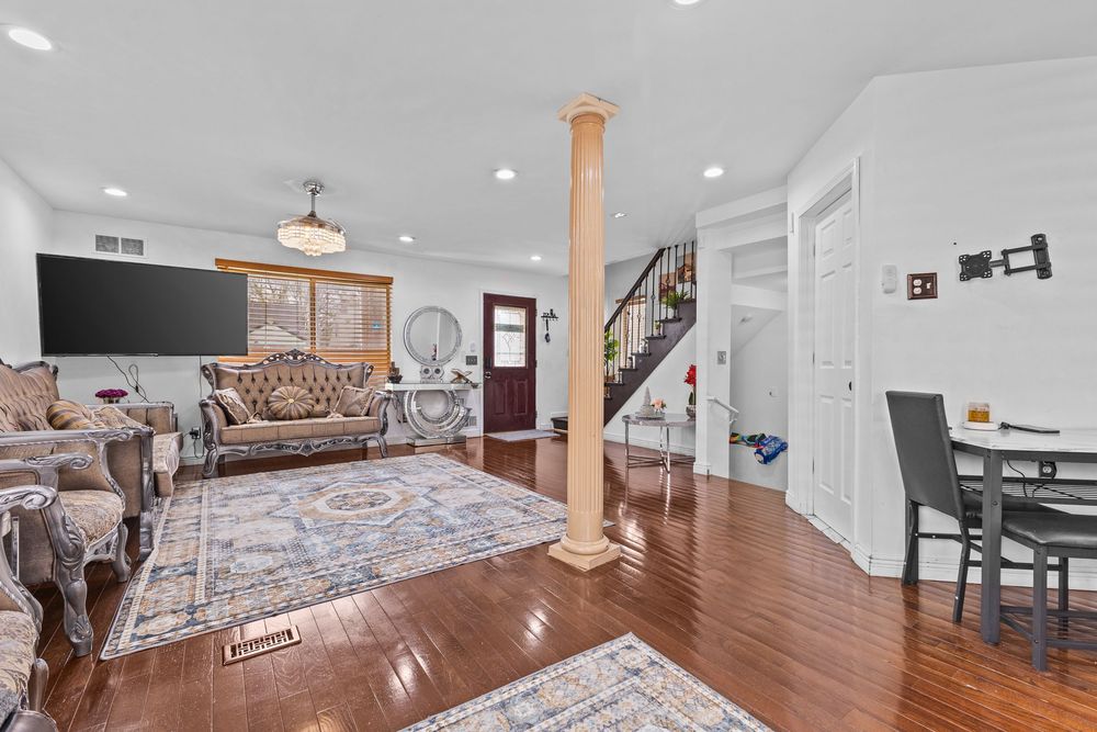 Bright living room featuring hardwood floors, ornate furniture, decorative column, recessed lighting, and staircase.