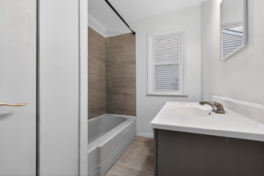 Modern bathroom with a tiled shower-tub combo, gray vanity, white countertop, and a bright window.