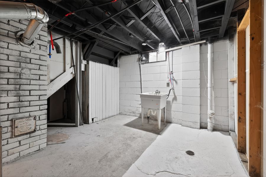 Unfinished basement with concrete block walls, exposed ceiling joists, utility sink, and concrete floor.