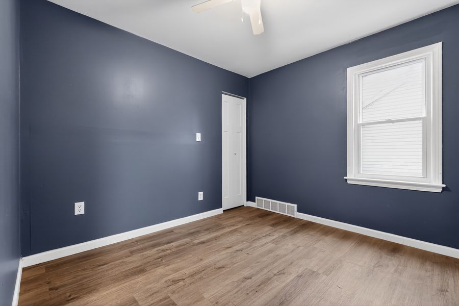 Empty room with navy blue walls, white trim, hardwood floors, and a window with blinds.