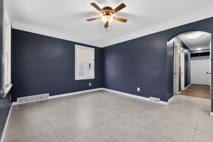 Empty room with navy blue walls, ceiling fan, tile floors, and an arched doorway leading to a hallway.