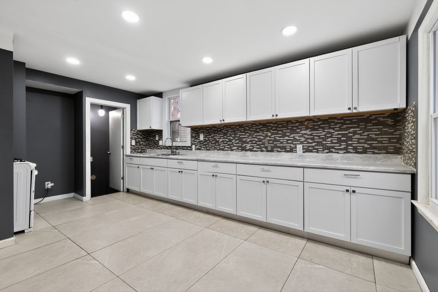 Modern kitchen with white shaker cabinets, mosaic tile backsplash, and large light gray porcelain floor tiles.
