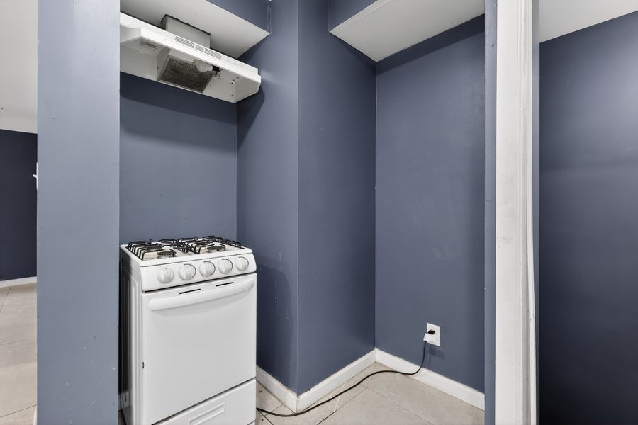 White gas stove in a compact navy blue kitchen nook with tile flooring and open shelving above.