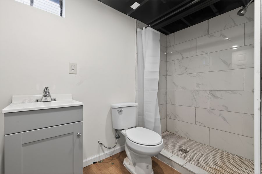 Modern bathroom with marble tile shower, white vanity, toilet, and dark ceiling accents.
