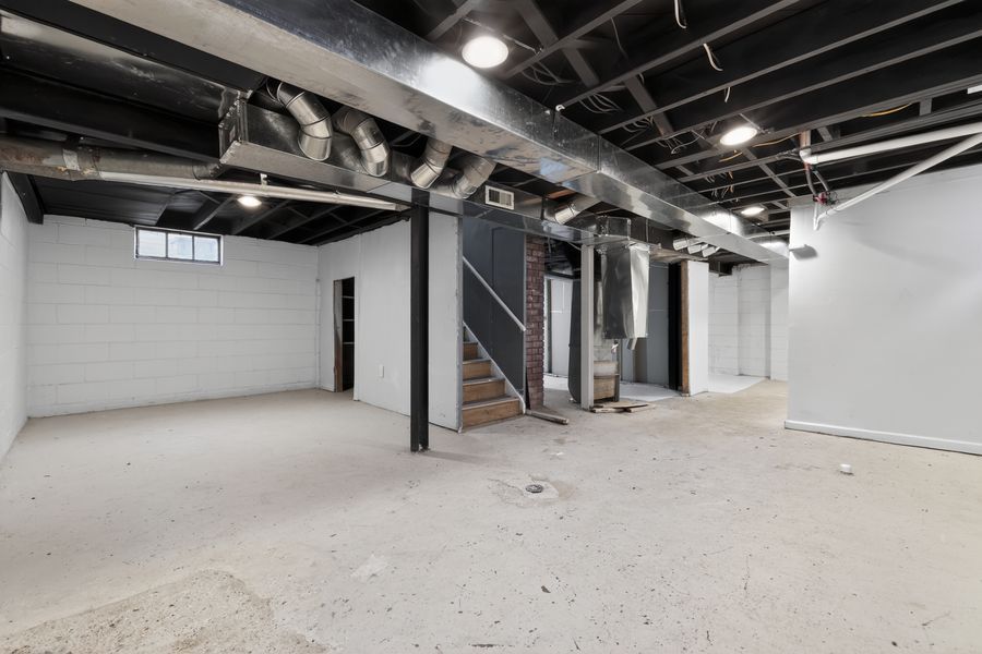 Unfinished basement with exposed ductwork, concrete floors, white walls, and open layout with staircase.
