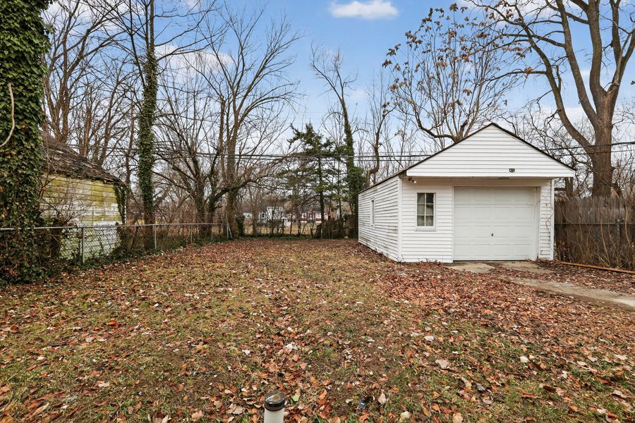 Detached white garage with large backyard covered in fallen leaves and surrounded by wooden fencing.