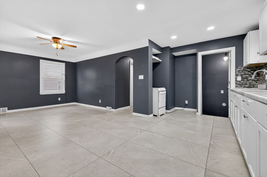 Spacious living area with large gray tiles, dark gray walls, arched doorways, recessed lighting, and a ceiling fan.