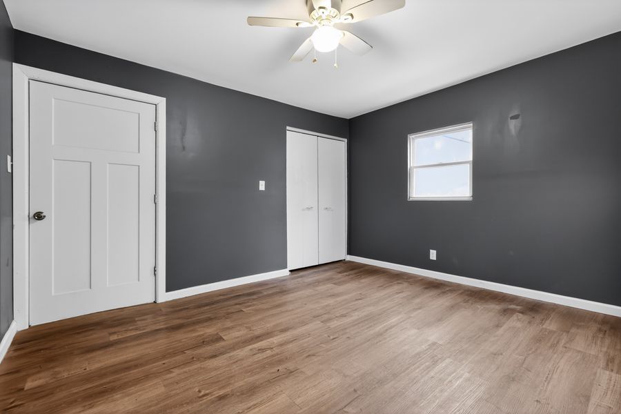 Spacious bedroom with dark gray walls, hardwood floors, white doors, and a ceiling fan.