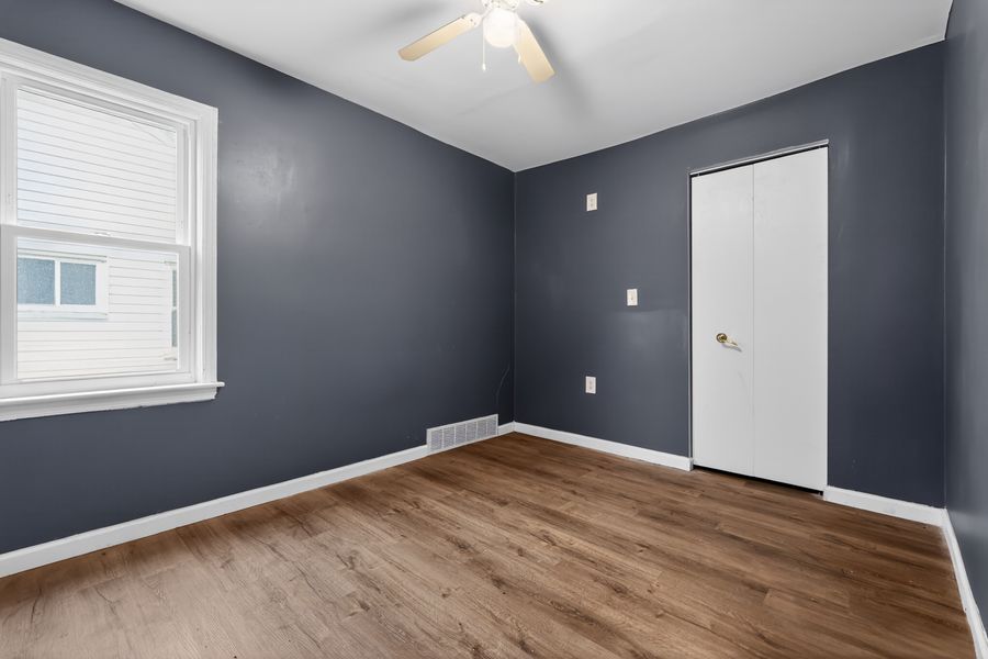 Empty bedroom with navy blue walls, hardwood floors, ceiling fan, and white baseboards.
