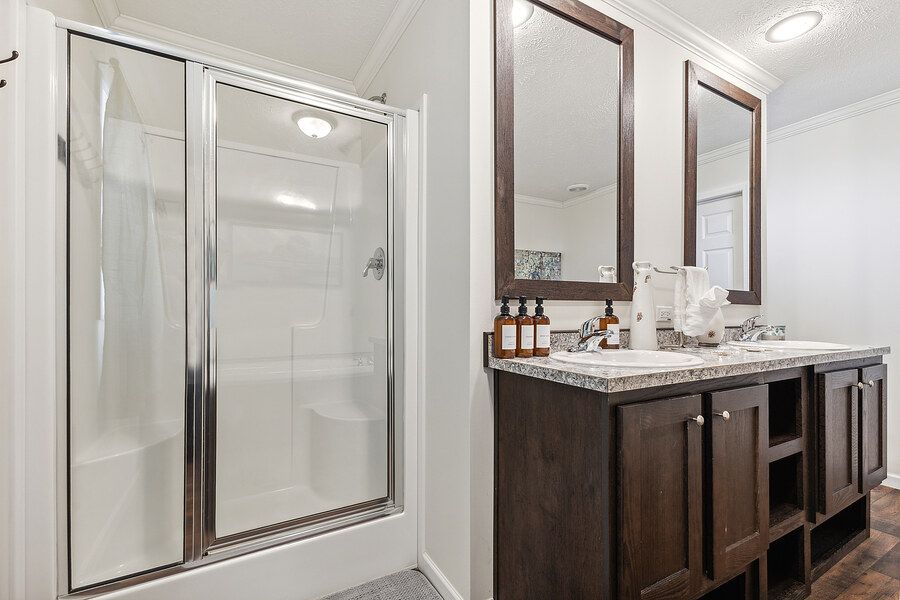 Bathroom with dark wood double vanity, granite countertops, framed mirrors, and a walk-in glass shower.