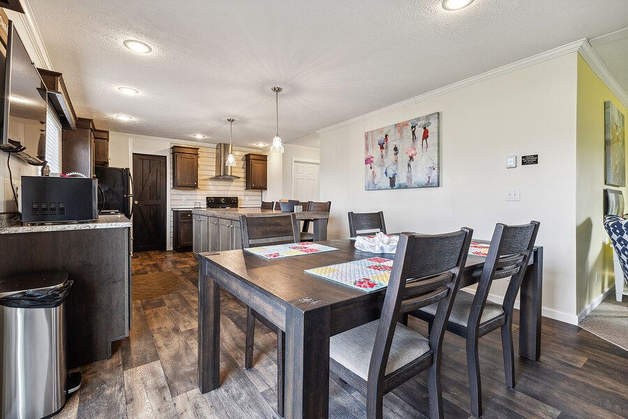 Modern open-concept dining area with dark wood table, chairs, and hardwood floors leading to a contemporary kitchen.
