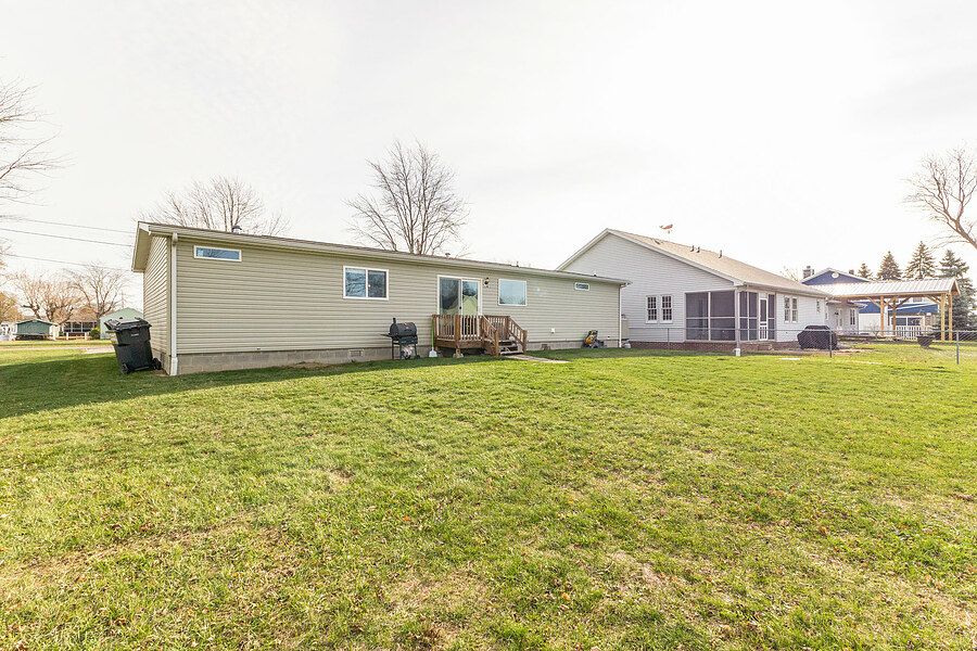 Spacious backyard with lush green lawn, tan ranch-style home, and screened porch addition under a cloudy sky.