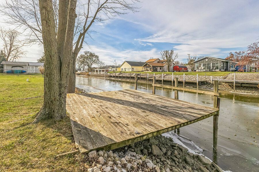 Wooden dock extending into a calm canal with lush green lawn and residential homes visible in the background.