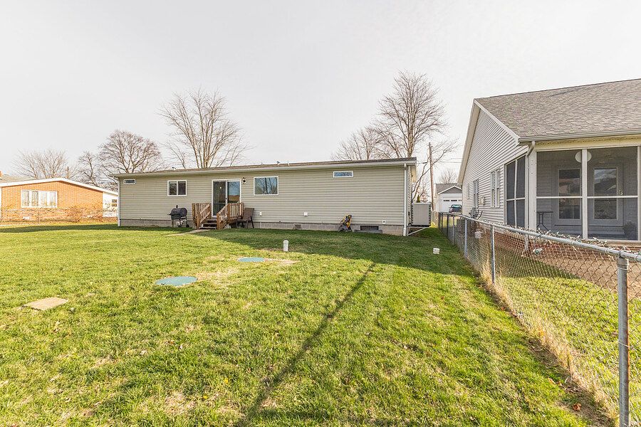 Backyard view of a ranch-style home with green lawn, chain-link fence, and neighboring houses under overcast skies.