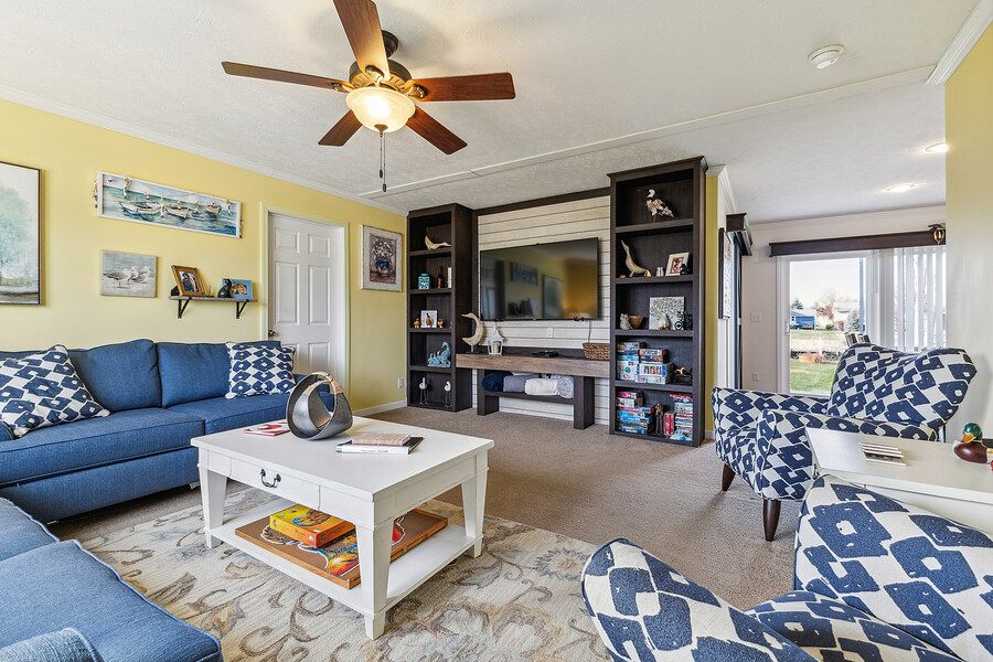Cozy living room with blue sofas, white coffee table, built-in entertainment center, ceiling fan, and yellow walls.