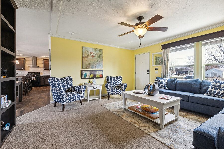 Cozy living room with blue sofa, patterned chairs, wood coffee table, ceiling fan, and bright window.