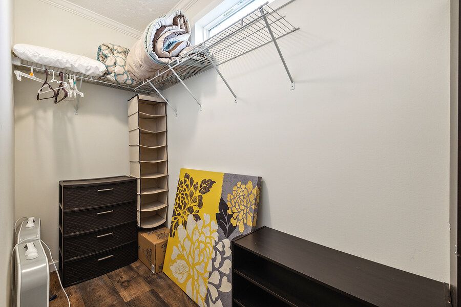 Walk-in closet with wire shelving, dark dresser, bench, and hardwood floors for ample storage.