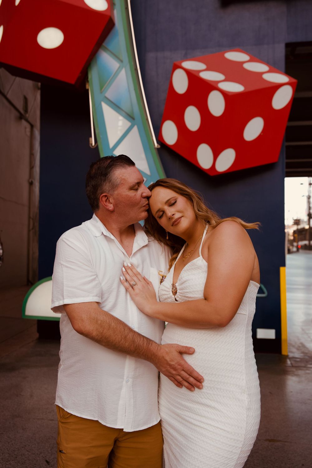 Couple embracing in front of giant red dice at the Neon Museum in Las Vegas, wearing white outfits.