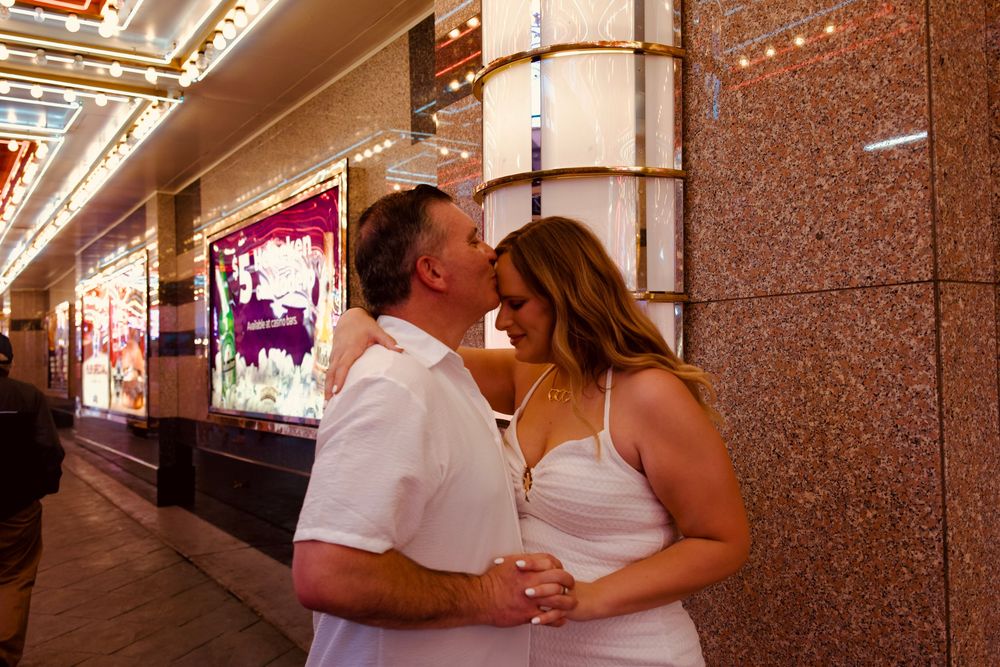 Couple sharing a kiss outside a glowing Las Vegas casino with marquee lights in the background.