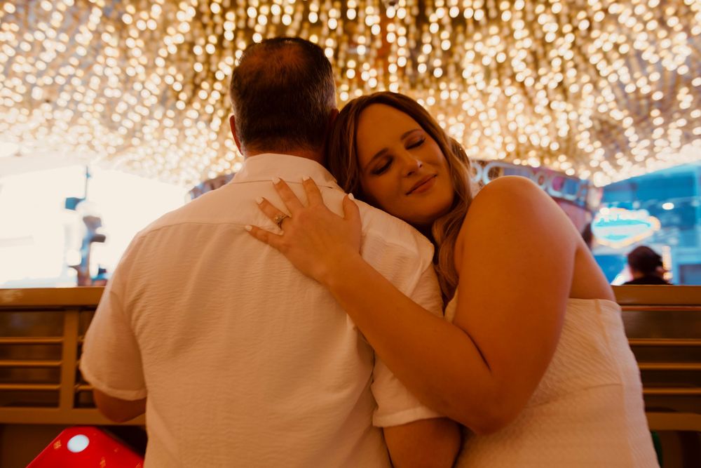 Couple embracing romantically under sparkling fairy lights at a Disney venue, woman in white dress leaning on mans shoulder.