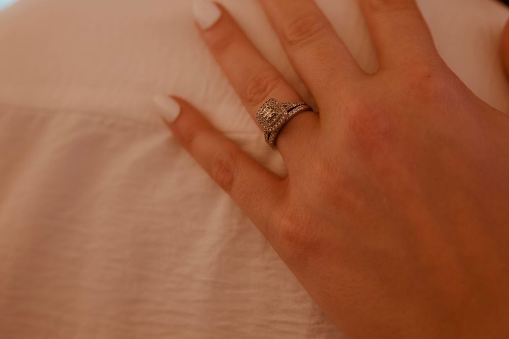 Close-up of a woman's hand wearing a diamond engagement ring and wedding band on a white background.