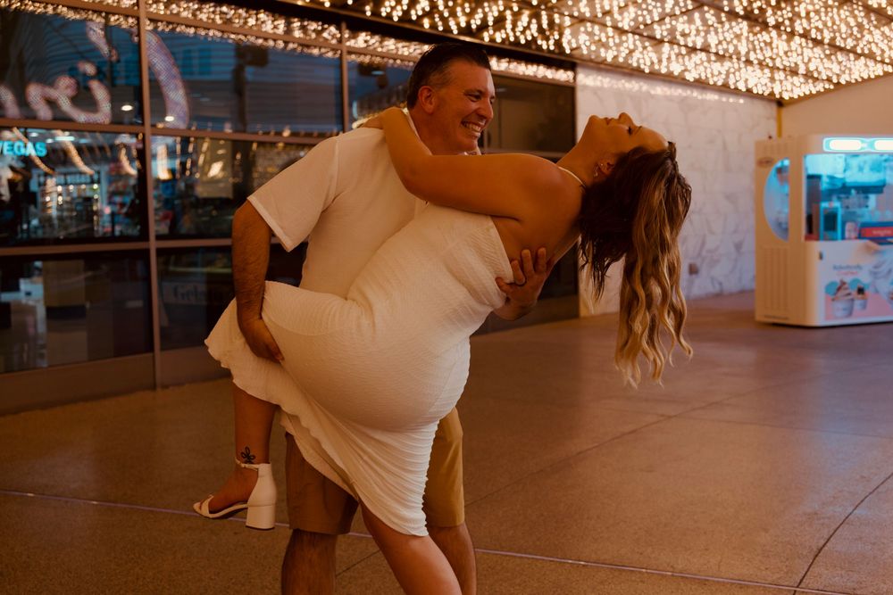 Couple in white outfits dancing joyfully under sparkling lights at a Las Vegas venue.