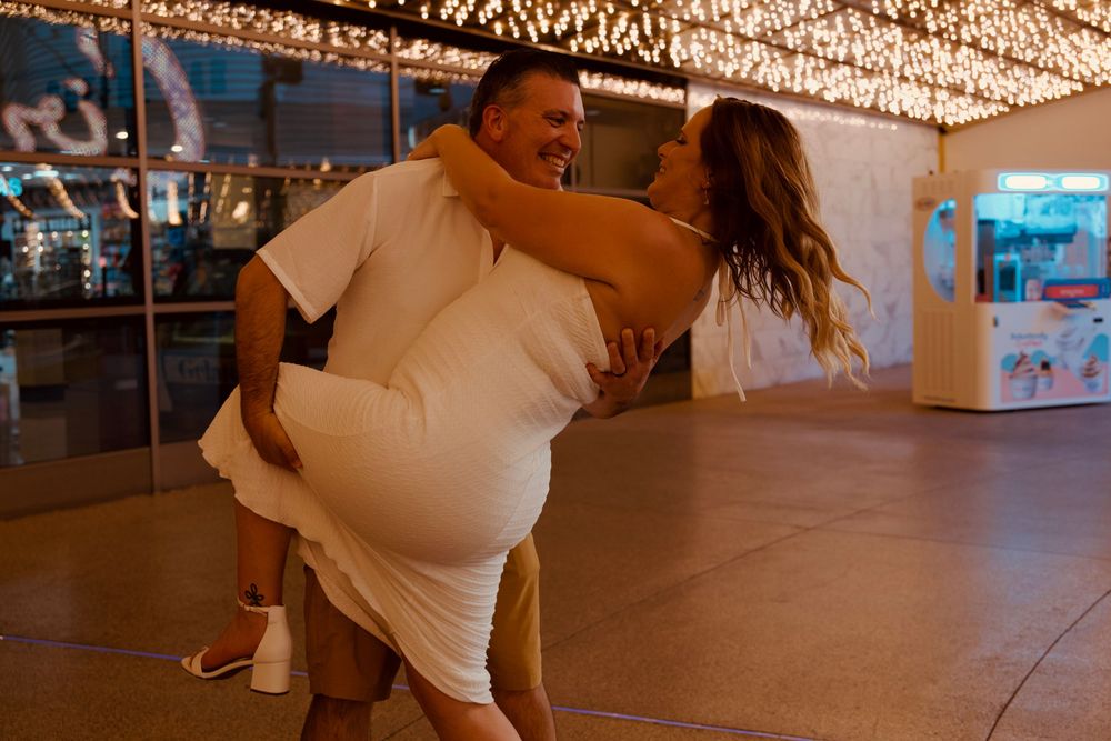 A joyful couple celebrating their wedding, with the groom lifting the bride in a white dress under warm string lights.