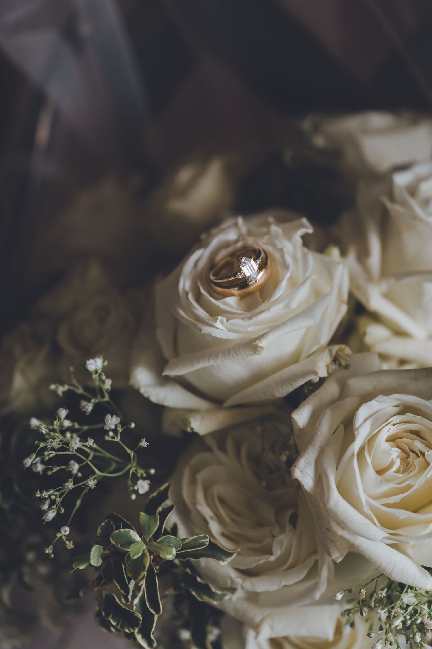 Gold wedding rings resting on white roses and baby's breath in an elegant bridal bouquet.