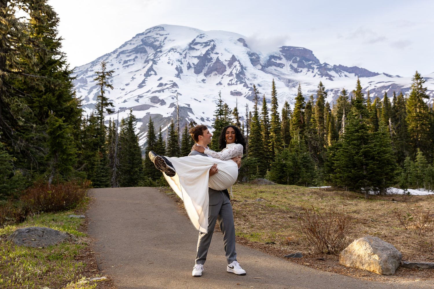 LGBTQ Elopement couple raising bouquets by a rushing forest river.