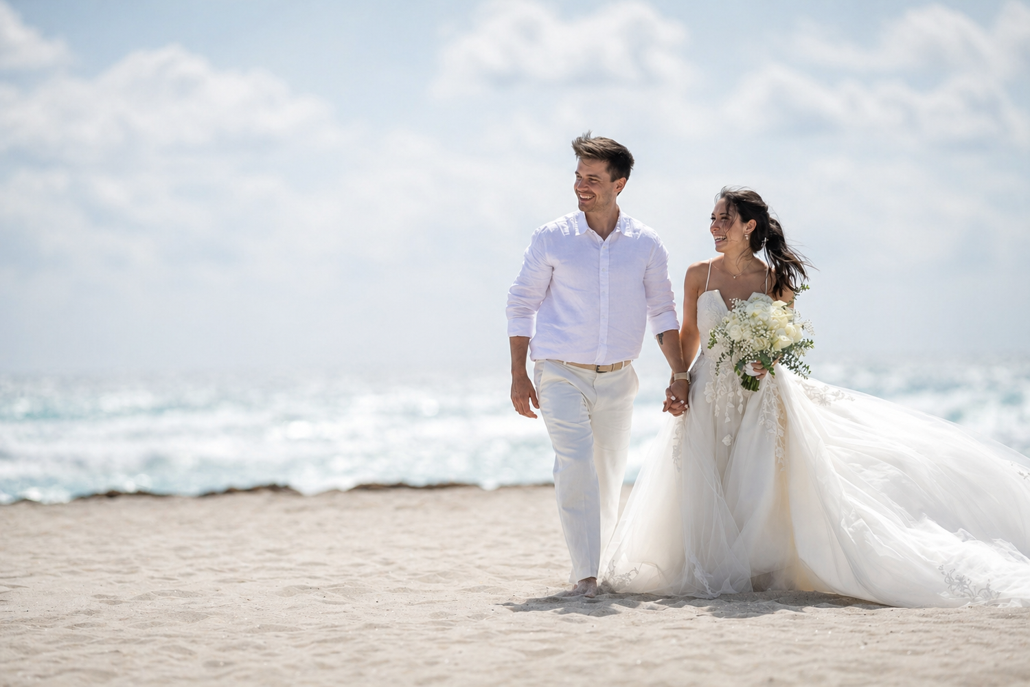 Bride in white gown holds colorful bouquet on elegant white balcony with gazebo and palm trees at outdoor wedding venue.