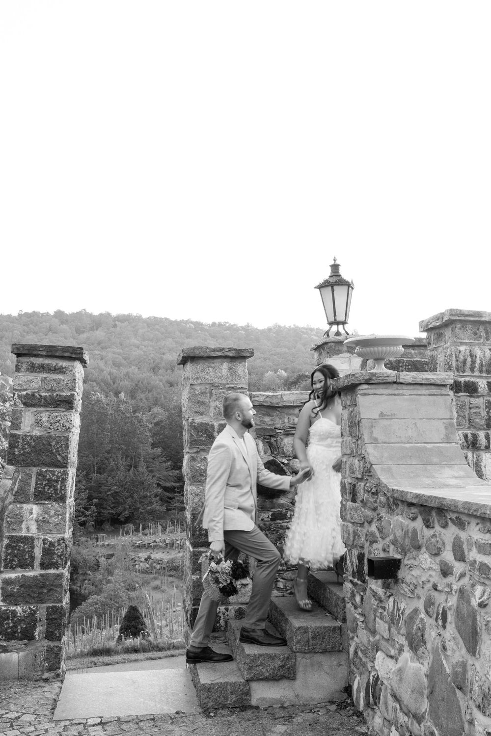 Black and white photo of bride and groom holding hands on stone steps at elegant castle wedding venue.
