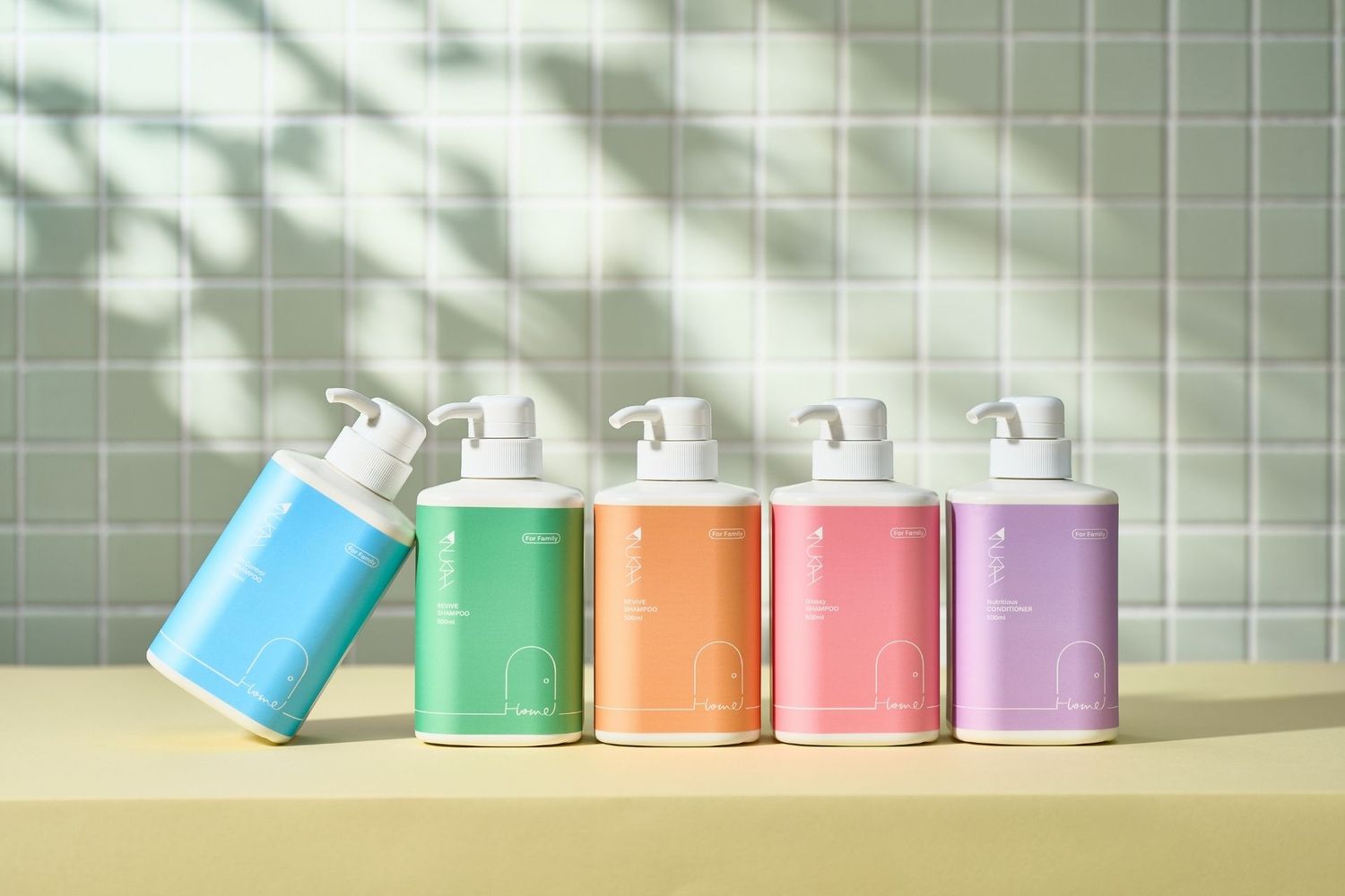 Five colorful pump dispenser bottles in blue, green, orange, white, and lavender arranged on a yellow shelf against a tiled wall.