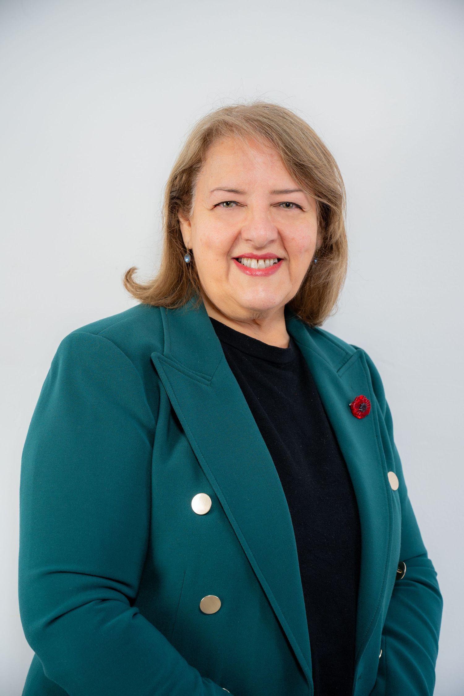Professional woman in teal blazer with red brooch smiling confidently against light gray background.