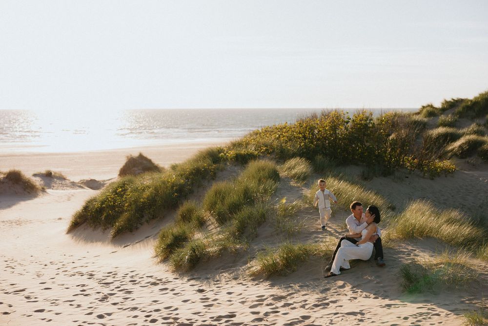 Couple sitting together on sandy beach dunes with ocean view on a sunny day.