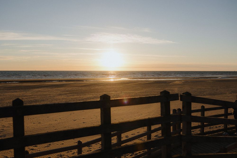 Golden sunset over calm ocean beach with wooden fence silhouette in foreground.