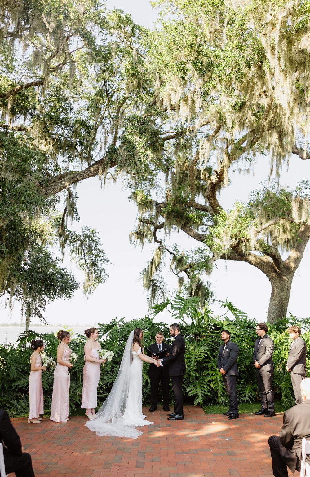 Bride and groom exchange vows under Spanish moss-draped oak trees at an elegant outdoor waterfront wedding ceremony.