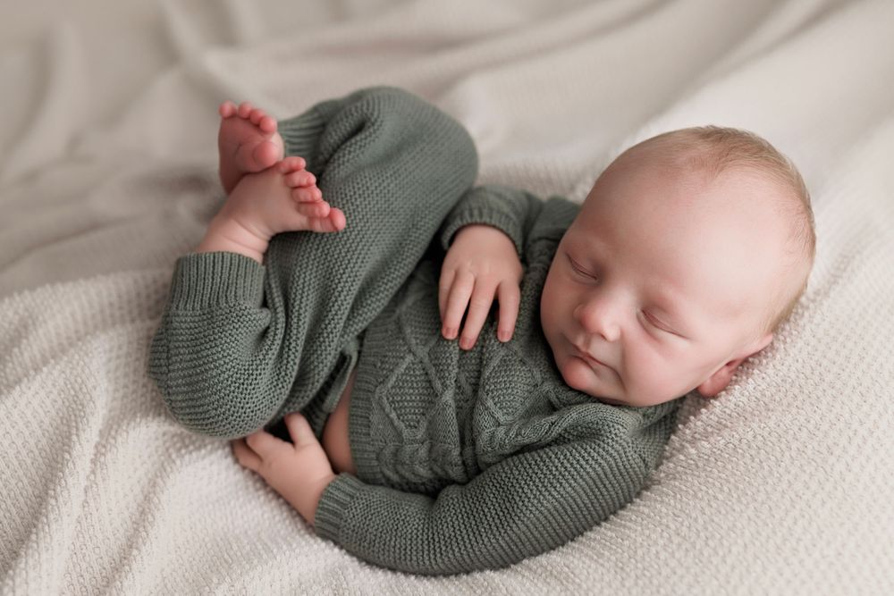 Sleeping newborn baby in green knit outfit lying on white blanket.